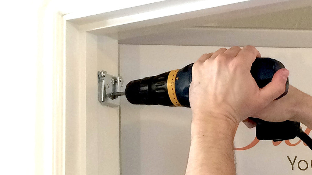 The image is showing a man is holding a drill installing doorway bar brackets.