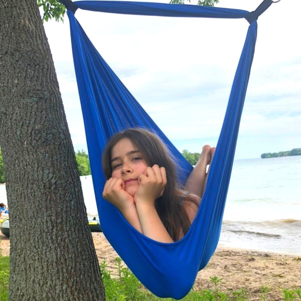 A girl is resting in a sensory swing hanged between two trees on a beach