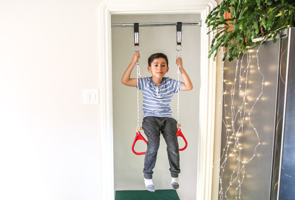 Doorway Swing - Installed right in a door frame - A boy is using a trapeze bar and rings combo attached to a swing support bar. 