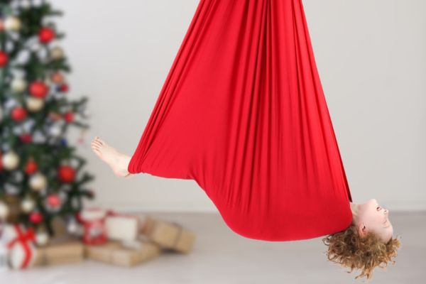 A boy is in a red sensory swing near a christmas tree.