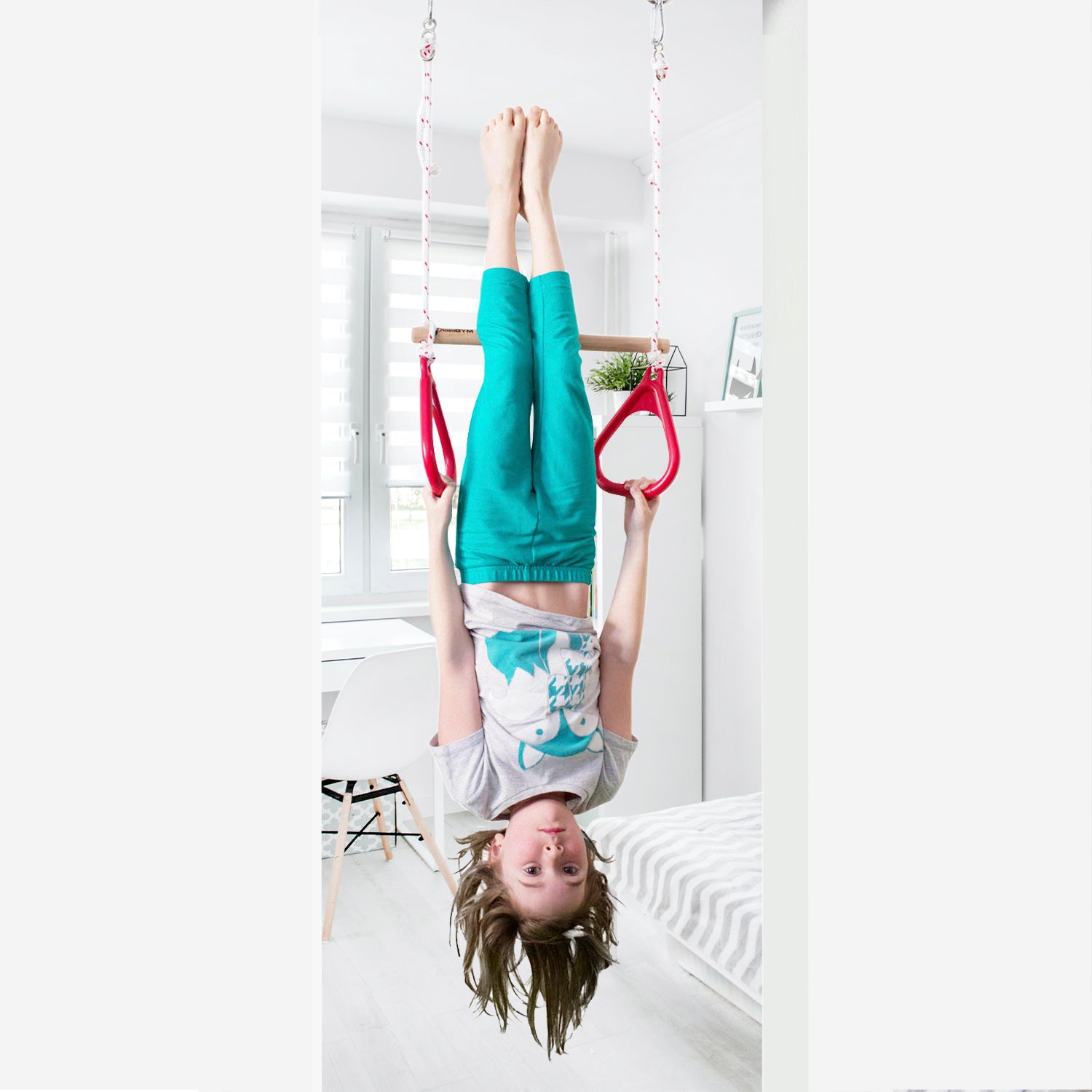 A girl is hanging upside down on a doorway trapeze bar and gymnastics rings combo