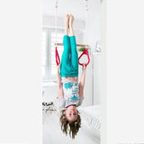 A girl is hanging upside down on a doorway trapeze bar and gymnastics rings combo