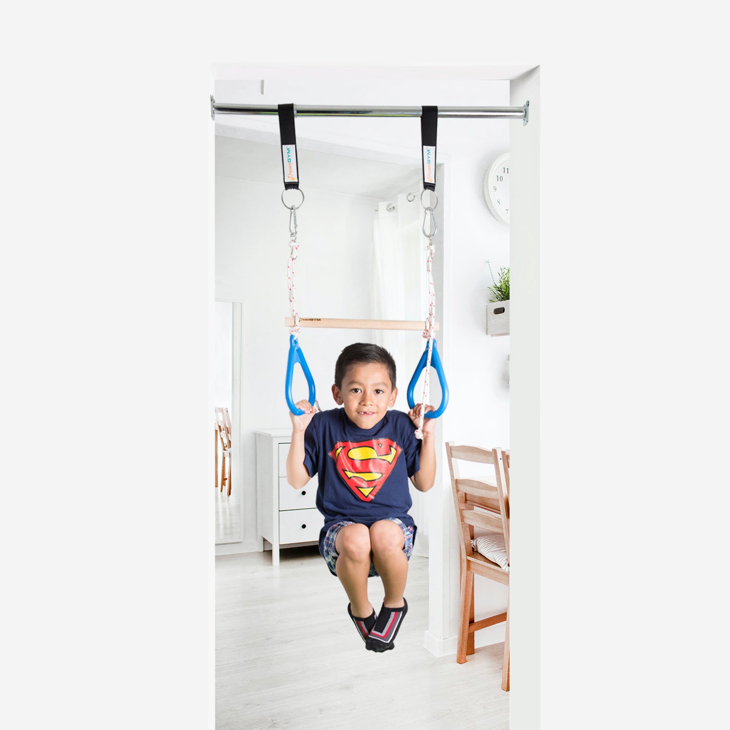 A  boy is playing on doorway gym. He pulled himself up on the trapeze bar and gymnastics rings combo.