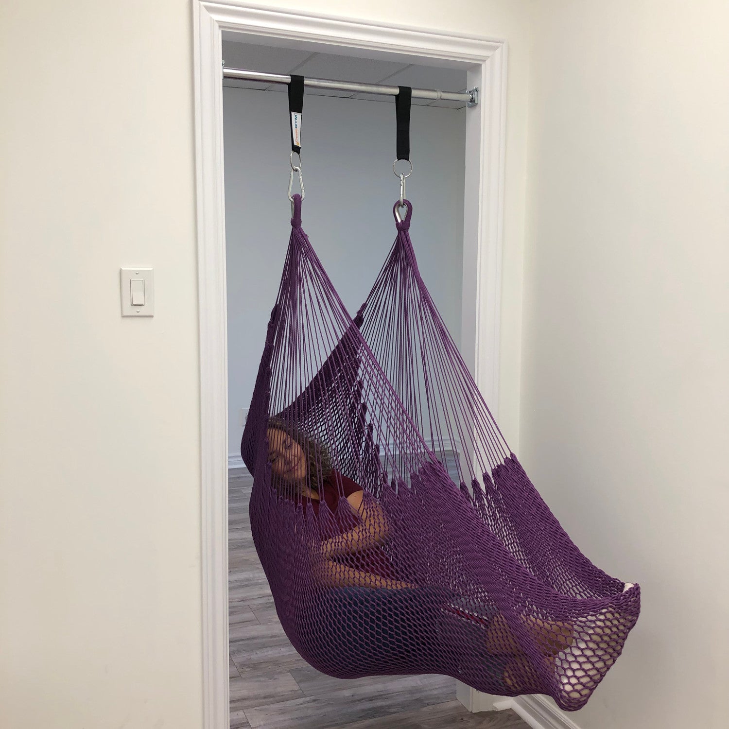 A woman is relaxing in a purple hammock swing installed in a door frame.