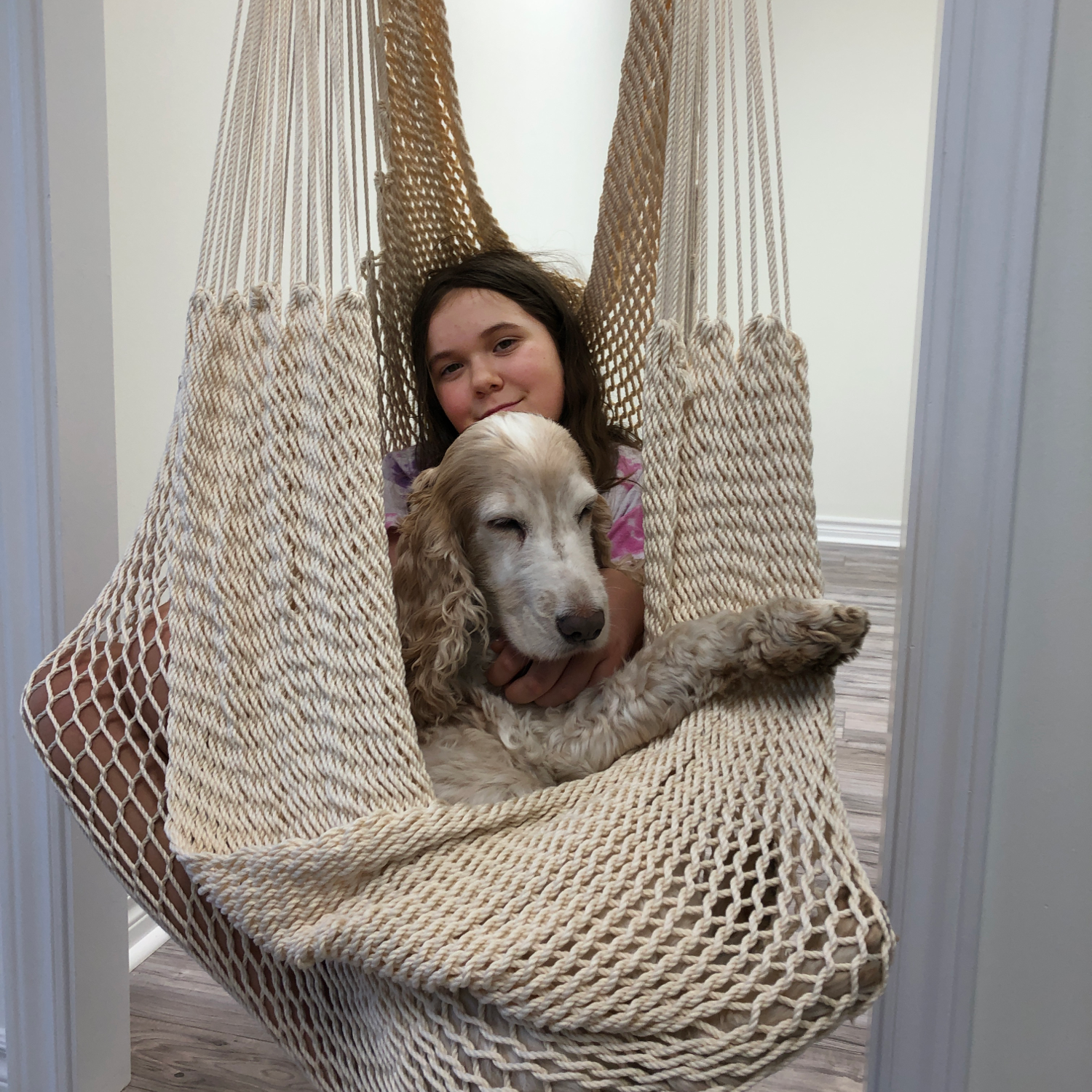 A girl and her puppy are sitting in a hammock swing installed in the doorway.