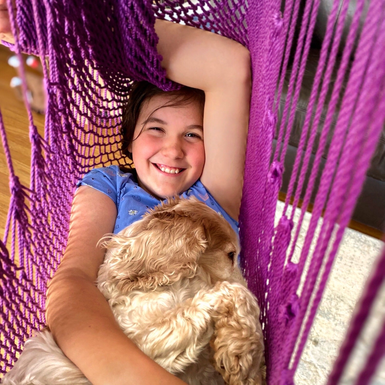 A happy girl is playing in a purple hammock swing with her dog.