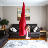 DreamGYM sensory swing. A happy girl is sitting inside a red sensory swing attached to the ceiling in a living room.